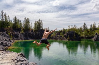 Atletik ve Maceracı Adam sıcak ve güneşli bir yaz gününde Yeşil Renkli Buzul Gölü içine Cliff Jumping olduğunu. British Columbia, Kanada'da çekilmiş.