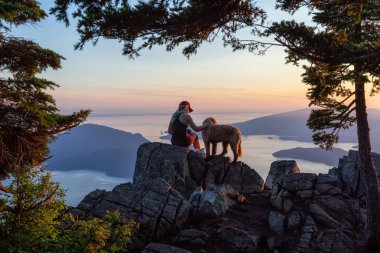 Adventurous Girl is hiking with a dog on top of St. Mark's Mountain during a sunny summer sunset. Located in West Vancouver, British Columbia, Canada. clipart