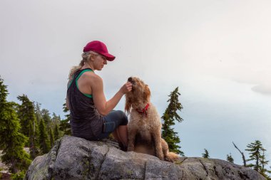 Maceracı Kız güneşli ve bulutlu bir yaz gününde Gereksiz Dağ tepesinde bir köpek ile yürüyüş olduğunu. Batı Vancouver, British Columbia, Kanada'da bulunan.