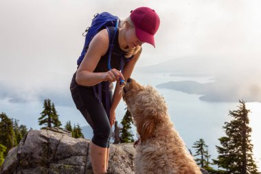 Maceracı Woman Hiker ve köpek bulutlu ve güneşli bir yaz gününde su dinking vardır. Vancouver, British Columbia, Kanada yakınlarındaki bir dağda yürüyüş yaparken çekilen.