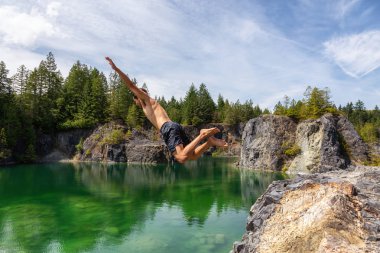 Atletik ve Maceracı Adam sıcak ve güneşli bir yaz gününde Yeşil Renkli Buzul Gölü içine Cliff Jumping olduğunu. British Columbia, Kanada'da çekilmiş.