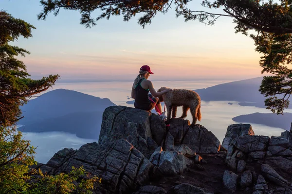 Adventurous Girl is hiking with a dog on top of St. Mark\'s Mountain during a sunny summer sunset. Located in West Vancouver, British Columbia, Canada.