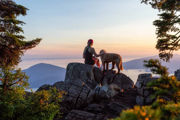 Adventurous Girl is hiking with a dog on top of St. Mark\'s Mountain during a sunny summer sunset. Located in West Vancouver, British Columbia, Canada.