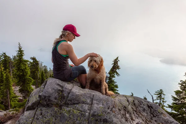 Adventurous Girl is hiking with a dog on top of Unnecessary Mountain during a sunny and cloudy summer day. Located in West Vancouver, British Columbia, Canada.