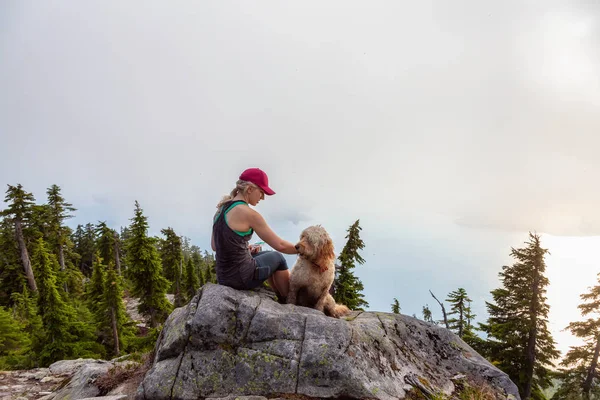 Adventurous Girl is hiking with a dog on top of Unnecessary Mountain during a sunny and cloudy summer day. Located in West Vancouver, British Columbia, Canada.