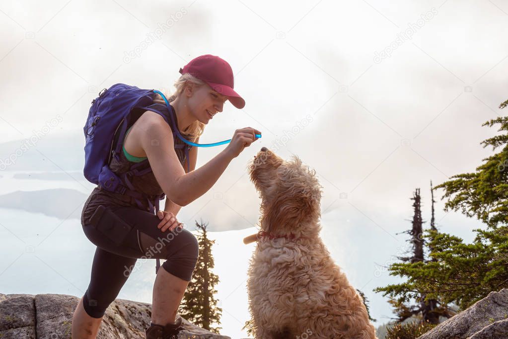 Adventurous Woman Hiker and dog are dinking water during a cloudy and sunny summer day. Taken while hiking on a mountain near Vancouver, British Columbia, Canada.