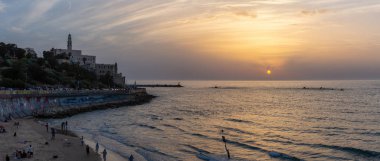 Tel Aviv, İsrail - 3 Nisan 2019: Güneşli ve renkli bir gün batımı sırasında Eski Yafa Limanı'ndaki bir plajın panoramik manzarası.
