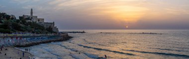 Tel Aviv, İsrail - 3 Nisan 2019: Güneşli ve renkli bir gün batımı sırasında Eski Yafa Limanı'ndaki bir plajın panoramik manzarası.