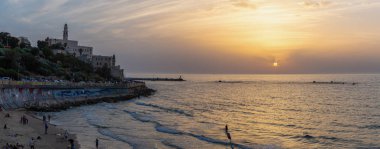 Tel Aviv, İsrail - 3 Nisan 2019: Güneşli ve renkli bir gün batımı sırasında Eski Yafa Limanı'ndaki bir plajın panoramik manzarası.