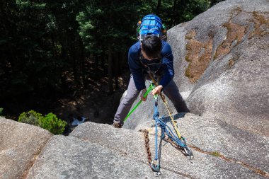 Rock Climber güneşli bir yaz günü boyunca sarp bir uçurumdan aşağı Rappeling olduğunu. Squamish, British Columbia, Kanada'da çekildi.