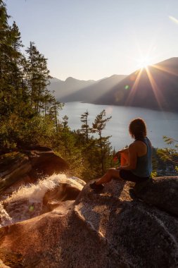 Maceracı Kız güzel bir şelale, Shannon Şelalesi üstünde oturuyor ve gün batımını izliyor. Squamish yakınlarında çekilmiş, Vancouver'ın kuzeyi, British Columbia, Kanada.