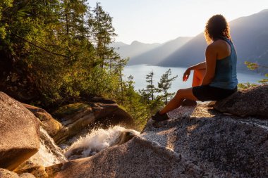 Maceracı Kız güzel bir şelale, Shannon Şelalesi üstünde oturuyor ve gün batımını izliyor. Squamish yakınlarında çekilmiş, Vancouver'ın kuzeyi, British Columbia, Kanada.