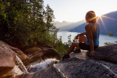 Maceracı Kız güzel bir şelale, Shannon Şelalesi üstünde oturuyor ve gün batımını izliyor. Squamish yakınlarında çekilmiş, Vancouver'ın kuzeyi, British Columbia, Kanada.