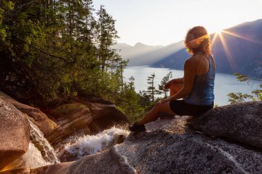Maceracı Kız güzel bir şelale, Shannon Şelalesi üstünde oturuyor ve gün batımını izliyor. Squamish yakınlarında çekilmiş, Vancouver'ın kuzeyi, British Columbia, Kanada.