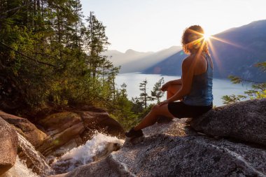 Maceracı Kız güzel bir şelale, Shannon Şelalesi üstünde oturuyor ve gün batımını izliyor. Squamish yakınlarında çekilmiş, Vancouver'ın kuzeyi, British Columbia, Kanada.