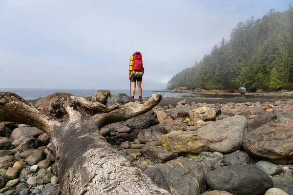Adventurous girl hiking Juan de Fuca Trail to Bear Beach on the Pacific Ocean Coast during a sunny and foggy summer morning. Taken near Port Renfrew, Vancouver Island, BC, Canada.