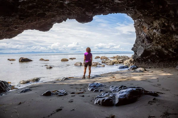 Adventurous girl hiking in a cave on Juan de Fuca Trail to Mystic Beach on the Pacific Ocean Coast during a sunny summer day. Taken near Port Renfrew, Vancouver Island, BC, Canada.
