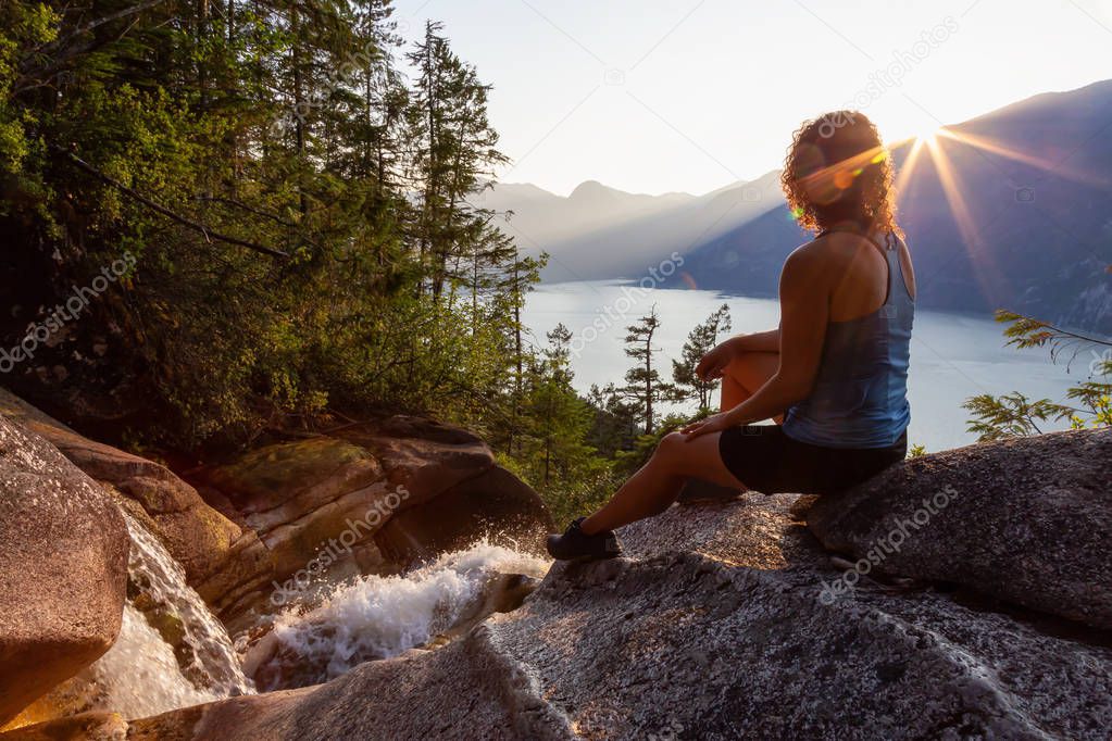Adventurous Girl is sitting on top of a Beautiful Waterfall, Shannon Falls, and watching the sunset. Taken near Squamish, North of Vancouver, British Columbia, Canada.