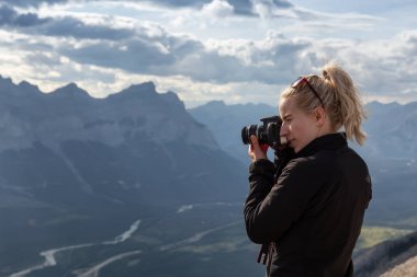 Canmore, Alberta, Kanada - 13 Ağustos 2019: Macera kadın Fotoğrafçı bulutlu bir gün boyunca kayalık bir dağın tepesinde fotoğraf çekiyor.