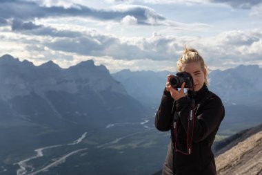 Canmore, Alberta, Kanada - 13 Ağustos 2019: Macera kadın Fotoğrafçı bulutlu bir gün boyunca kayalık bir dağın tepesinde fotoğraf çekiyor.