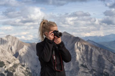 Canmore, Alberta, Kanada - 13 Ağustos 2019: Macera kadın Fotoğrafçı bulutlu bir gün boyunca kayalık bir dağın tepesinde fotoğraf çekiyor.