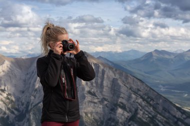 Canmore, Alberta, Kanada - 13 Ağustos 2019: Macera kadın Fotoğrafçı bulutlu bir gün boyunca kayalık bir dağın tepesinde fotoğraf çekiyor.