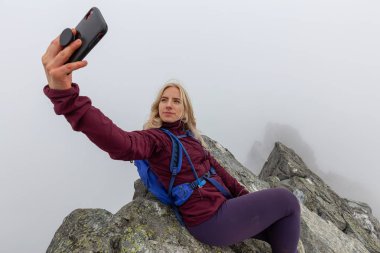 Genç Maceracı Kız bulutlu bir yaz sabahı bir selfie alarak engebeli kayalık dağın tepesinde. Crown Mountain'da çekilmiş, Kuzey Vancouver, Bc, Kanada.
