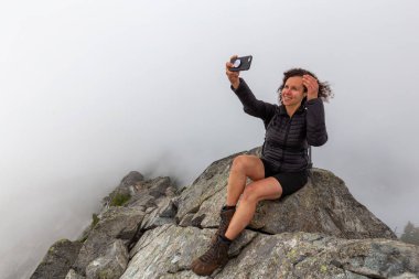 Genç Maceracı Kız bulutlu bir yaz sabahı bir selfie alarak engebeli kayalık dağın tepesinde. Crown Mountain'da çekilmiş, Kuzey Vancouver, Bc, Kanada.