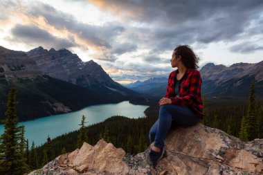 Maceracı kız canlı bir yaz gün batımı sırasında güzel Kanada Rockies ve Peyto Gölü bakan bir uçurumun kenarında oturuyor. Alınan Banff Ulusal Parkı, Alberta, Kanada.