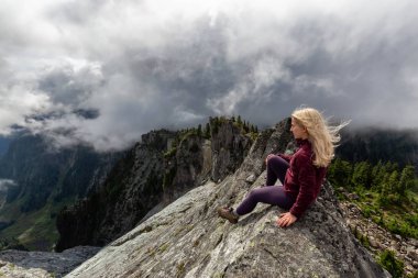 Bulutlu bir yaz sabahı engebeli kayalık dağın tepesinde Maceracı Kız. Crown Mountain'da çekilmiş, Kuzey Vancouver, Bc, Kanada.