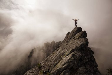 Bulutlu bir yaz sabahı engebeli kayalık dağın tepesinde Açık Kollu Maceracı Kız. Crown Mountain'da çekilmiş, Kuzey Vancouver, Bc, Kanada.