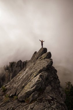 Bulutlu bir yaz sabahı engebeli kayalık dağın tepesinde Açık Kollu Maceracı Kız. Crown Mountain'da çekilmiş, Kuzey Vancouver, Bc, Kanada.