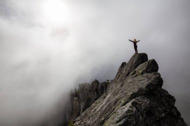 Bulutlu bir yaz sabahı engebeli kayalık dağın tepesinde Açık Kollu Maceracı Kız. Crown Mountain'da çekilmiş, Kuzey Vancouver, Bc, Kanada.