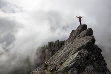 Bulutlu bir yaz sabahı engebeli kayalık dağın tepesinde Açık Kollu Maceracı Kız. Crown Mountain'da çekilmiş, Kuzey Vancouver, Bc, Kanada.