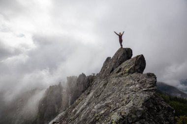 Bulutlu bir yaz sabahı engebeli kayalık dağın tepesinde Açık Kollu Maceracı Kız. Crown Mountain'da çekilmiş, Kuzey Vancouver, Bc, Kanada.