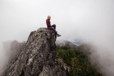 Bulutlu bir yaz sabahı engebeli kayalık dağın tepesinde Maceracı Kız. Crown Mountain'da çekilmiş, Kuzey Vancouver, Bc, Kanada.