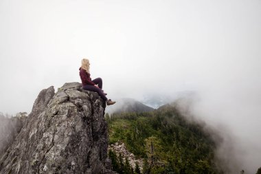 Bulutlu bir yaz sabahı engebeli kayalık dağın tepesinde Maceracı Kız. Crown Mountain'da çekilmiş, Kuzey Vancouver, Bc, Kanada.