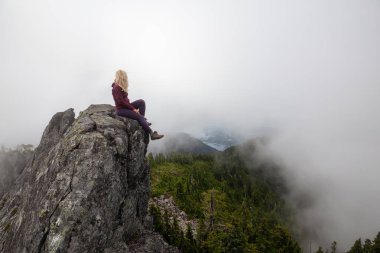 Bulutlu bir yaz sabahı engebeli kayalık dağın tepesinde Maceracı Kız. Crown Mountain'da çekilmiş, Kuzey Vancouver, Bc, Kanada.
