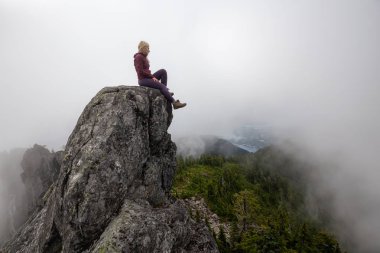 Bulutlu bir yaz sabahı engebeli kayalık dağın tepesinde Maceracı Kız. Crown Mountain'da çekilmiş, Kuzey Vancouver, Bc, Kanada.