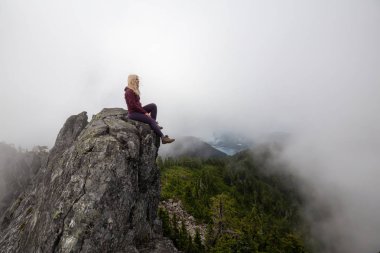 Bulutlu bir yaz sabahı engebeli kayalık dağın tepesinde Maceracı Kız. Crown Mountain'da çekilmiş, Kuzey Vancouver, Bc, Kanada.