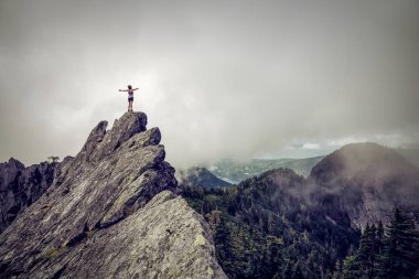 Bulutlu bir yaz sabahı engebeli kayalık dağın tepesinde Açık Kollu Maceracı Kız. Crown Mountain'da çekilmiş, Kuzey Vancouver, Bc, Kanada.