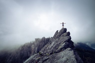 Bulutlu bir yaz sabahı engebeli kayalık dağın tepesinde Açık Kollu Maceracı Kız. Crown Mountain'da çekilmiş, Kuzey Vancouver, Bc, Kanada.