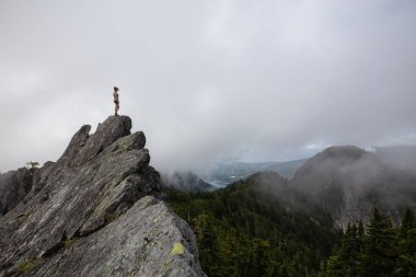 Bulutlu bir yaz sabahı engebeli kayalık dağın tepesinde Maceracı Kız. Crown Mountain'da çekilmiş, Kuzey Vancouver, Bc, Kanada.
