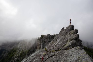 Maceracı Kız bulutlu bir yaz sabahı boyunca engebeli kayalık dağın üstüne parmak işaret. Crown Mountain'da çekilmiş, Kuzey Vancouver, Bc, Kanada.