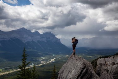 Maceracı Kız bulutlu ve yağmurlu bir gün boyunca kayalık bir dağın tepesinde fotoğraf çekmek. Lady Macdonald, Canmore, Alberta, Kanada'dan alındı.