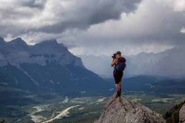 Maceracı Kız bulutlu ve yağmurlu bir gün boyunca kayalık bir dağın tepesinde fotoğraf çekmek. Lady Macdonald, Canmore, Alberta, Kanada'dan alındı.