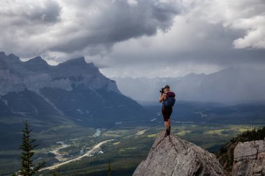 Maceracı Kız bulutlu ve yağmurlu bir gün boyunca kayalık bir dağın tepesinde fotoğraf çekmek. Lady Macdonald, Canmore, Alberta, Kanada'dan alındı.