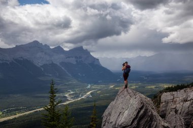 Maceracı Kız bulutlu ve yağmurlu bir gün boyunca kayalık bir dağın tepesinde fotoğraf çekmek. Lady Macdonald, Canmore, Alberta, Kanada'dan alındı.