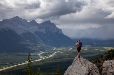 Maceracı Kız bulutlu ve yağmurlu bir gün boyunca kayalık bir dağın tepesinde fotoğraf çekmek. Lady Macdonald, Canmore, Alberta, Kanada'dan alındı.