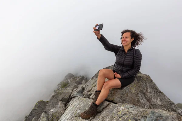 Genç Maceracı Kız bulutlu bir yaz sabahı bir selfie alarak engebeli kayalık dağın tepesinde. Crown Mountain'da çekilmiş, Kuzey Vancouver, Bc, Kanada.